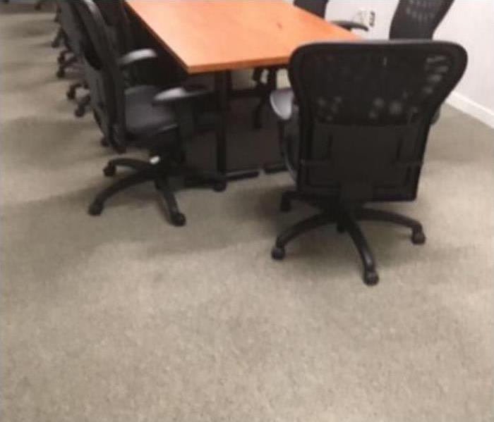 clean beige carpet with long wooden brown desk that sits multiple black chairs around it.