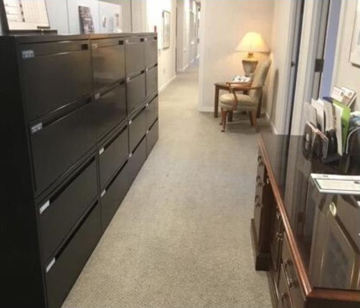 dirty beige carpet with black filing cabinet with multiple drawers to the left and brown desk to the right and chair