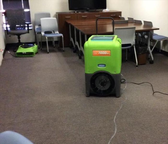conference room with wheeled chairs and tables pushed towards the back; green vacuum on the floor and other SERVPRO equipment