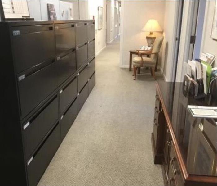 clean beige carpet with black filing cabinet with multiple drawers to the left and brown desk to the right and chair