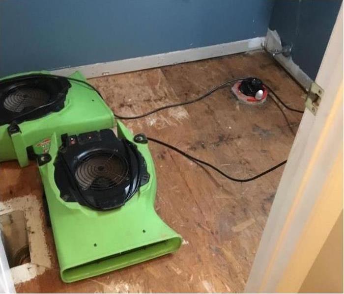torn up flooring with two green air scrubbers and a light colored wall.