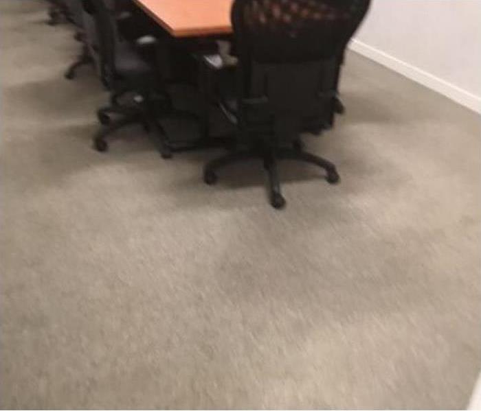 dirty beige carpet with long wooden brown desk that sits multiple black chairs around it.