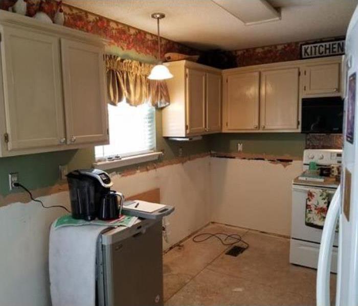 kitchen with cabinets torn out, window to the side, white stove in the background, white refrigerator at the front.
