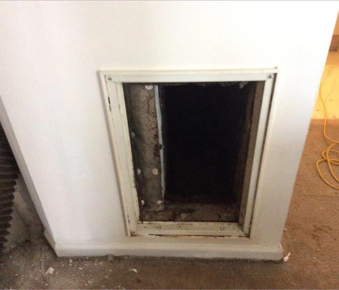 air vent cut out of a white wall surrounded by dirty brown carpet.