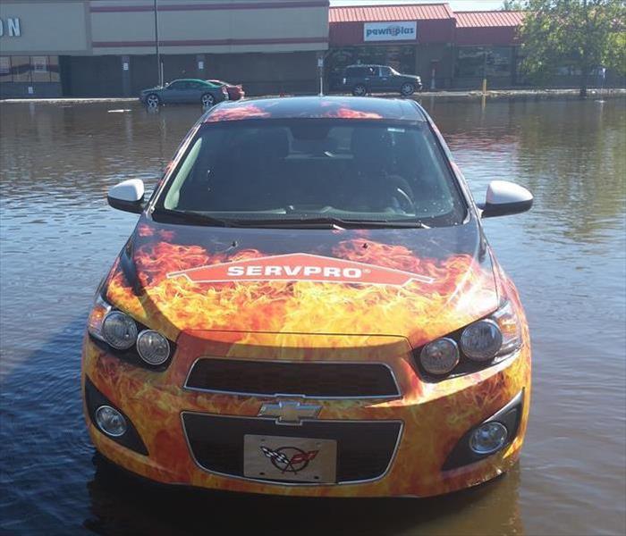 SERVPRO car surrounded by flood water in front of a building with a blue sky. 